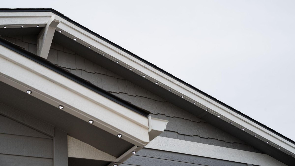 Daytime close-up of a roofline showing the low-profile track tucked under the eave with the lighting modules seated inside it.