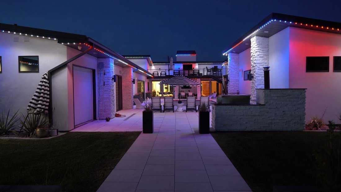 A modern home lit at night, with different colors running along separate rooflines and the patio area to show independent zone control.